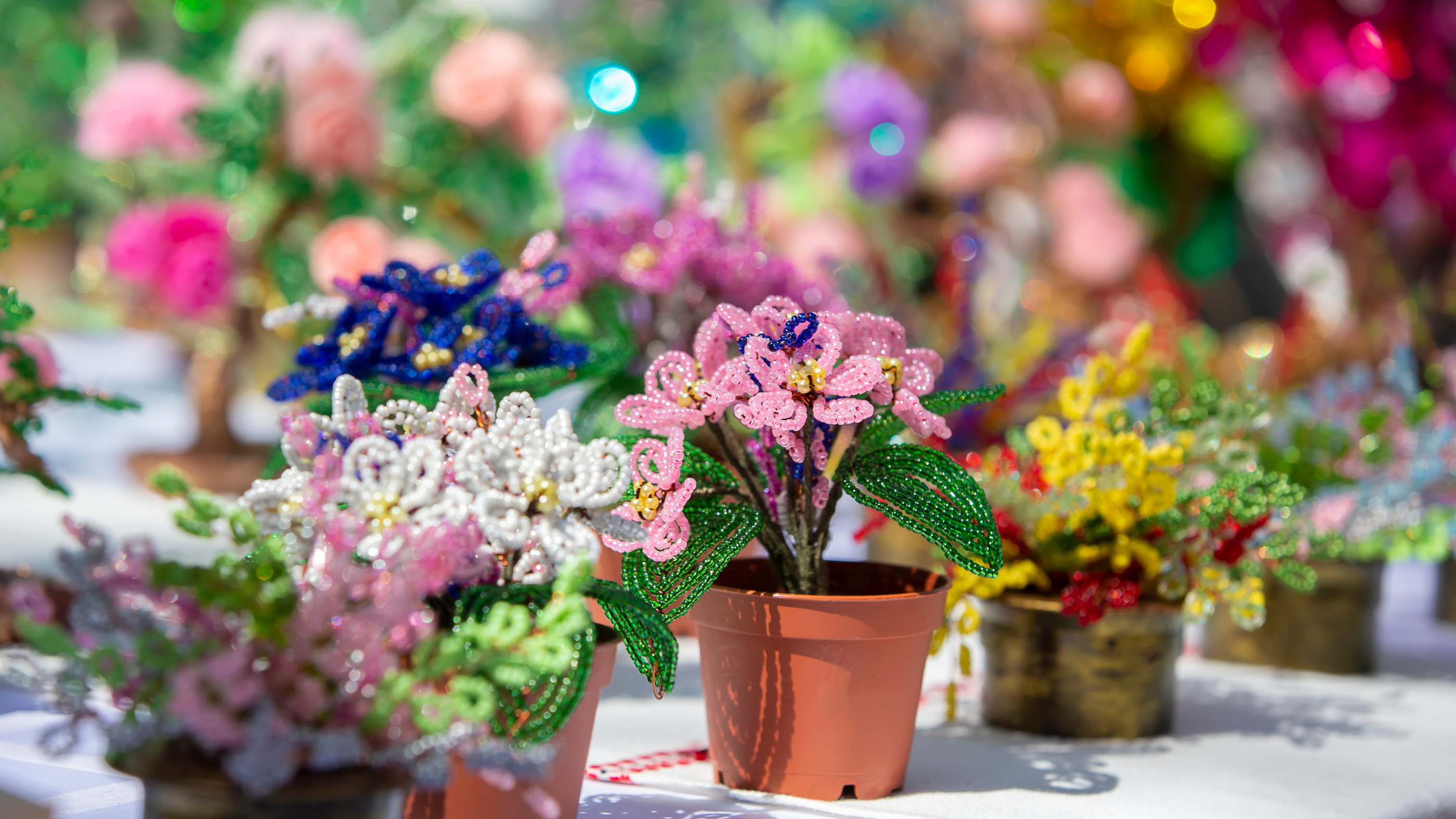 Colorful beaded flowers in small pots displayed on a table.