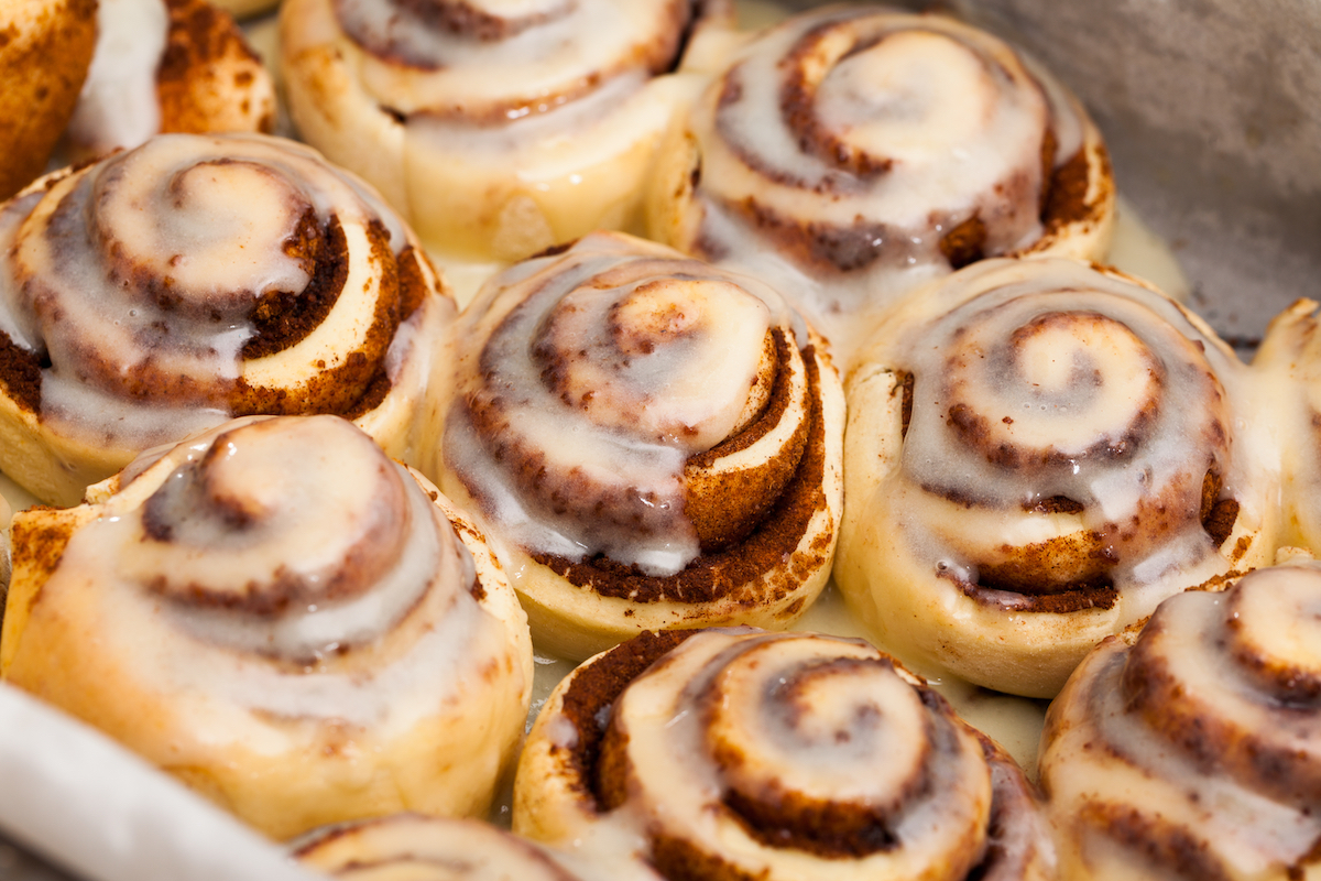 Freshly baked cinnamon rolls with white icing in a baking tray.