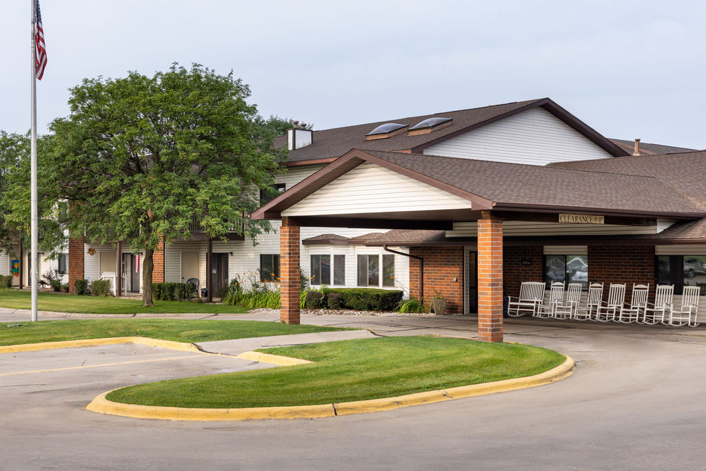 Single-story building with a covered entrance, rocking chairs on the porch, landscaped grounds, and an American flagpole in front. Single-story building with a covered entrance, rocking chairs on the porch, landscaped grounds, and an American flagpole in front.